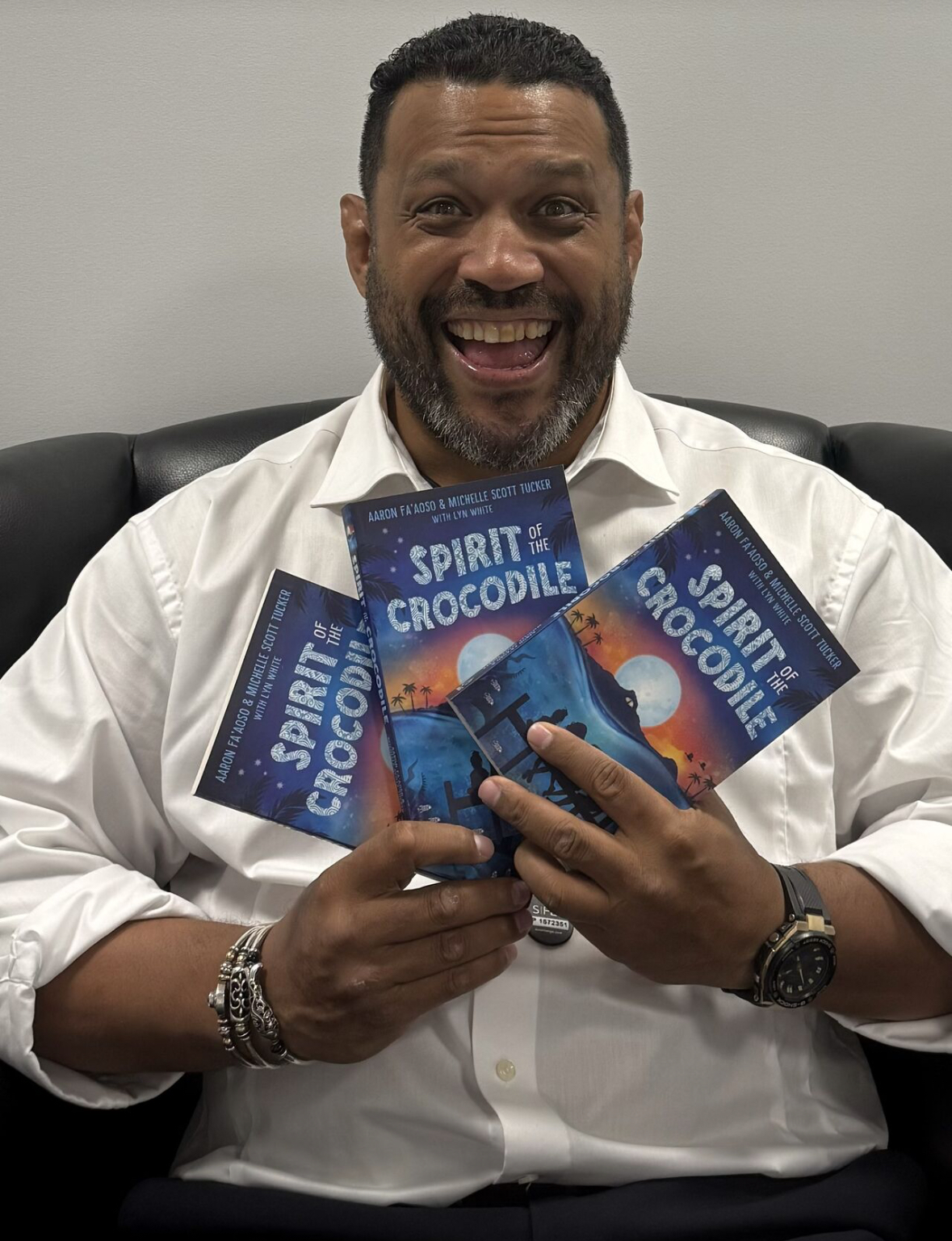Aaron Fa'Aoso, a Torres Strait Islander man, smiling widely and holding three copies of 'Spirit of the Crocodile'.